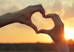 hands making hearth shape in front of sunset